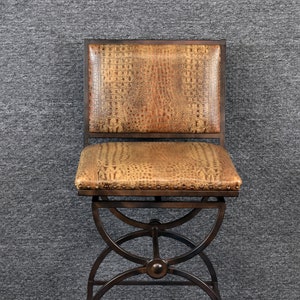 May include: A brown leather bar stool with a metal frame and a crocodile print design. The stool has a swivel seat and a footrest. The stool is on a gray carpet. The word "CARTHIA" is printed on the carpet.