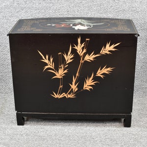 Pode incluir: Um arm&aacute;rio de madeira preto com um design de bambu dourado e um motivo floral na parte superior. O arm&aacute;rio tem forma quadrada e assenta em quatro pernas.