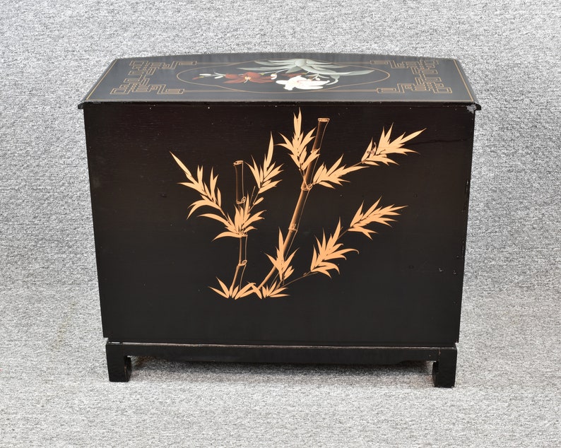 Pode incluir: Um arm&aacute;rio de madeira preto com um design de bambu dourado e um motivo floral na parte superior. O arm&aacute;rio tem forma quadrada e assenta em quatro pernas.