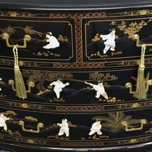 Pode incluir: Um ba&uacute; de gavetas lacado de preto com tr&ecirc;s gavetas. Cada gaveta tem uma pega dourada e um puxador com borla. As gavetas s&atilde;o decoradas com cenas pintadas a ouro e branco de pessoas numa paisagem.