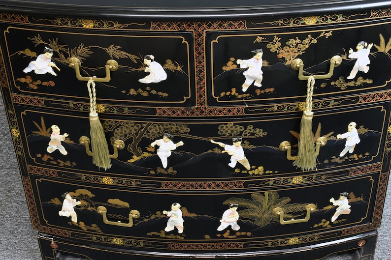 Pode incluir: Um ba&uacute; de gavetas lacado de preto com tr&ecirc;s gavetas. Cada gaveta tem uma pega dourada e um puxador com borla. As gavetas s&atilde;o decoradas com cenas pintadas a ouro e branco de pessoas numa paisagem.
