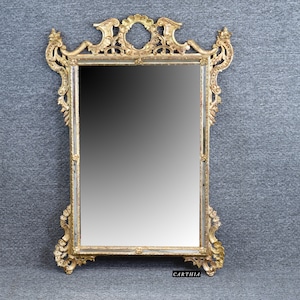 May include: A gold-toned ornate mirror with a rectangular frame and a beveled edge. The frame is intricately carved with floral and scroll designs.