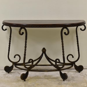 May include: A half-circle console table with a dark brown wooden top and ornate wrought iron base. The base features scrolled details and twisted supports, creating an elegant, vintage aesthetic. The table is designed for placement against a wall.