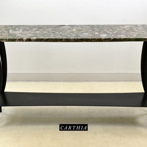 May include: A long, rectangular console table with a green and pink speckled marble top and a black metal base. The base has a lower shelf and curved legs.