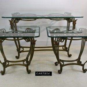 May include: A set of three glass-top tables with ornate metal frames. The tables are in a gold finish and have a scrolled design. The largest table is a console table, and the two smaller tables are end tables.