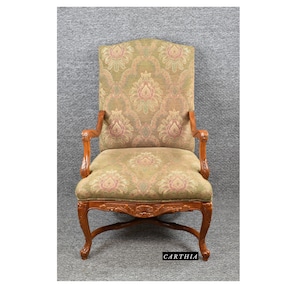 May include: A carved wooden armchair with a floral patterned fabric upholstery. The chair has a high back and curved arms. The chair is in a light wood tone with a green and pink floral pattern on the fabric.