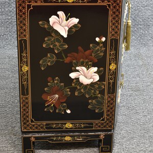 Pode incluir: Arm&aacute;rio lacado de preto com design floral. O arm&aacute;rio tem um motivo floral com flores rosa, brancas e marrons sobre um fundo preto. O arm&aacute;rio tem detalhes dourados e uma borla decorativa.