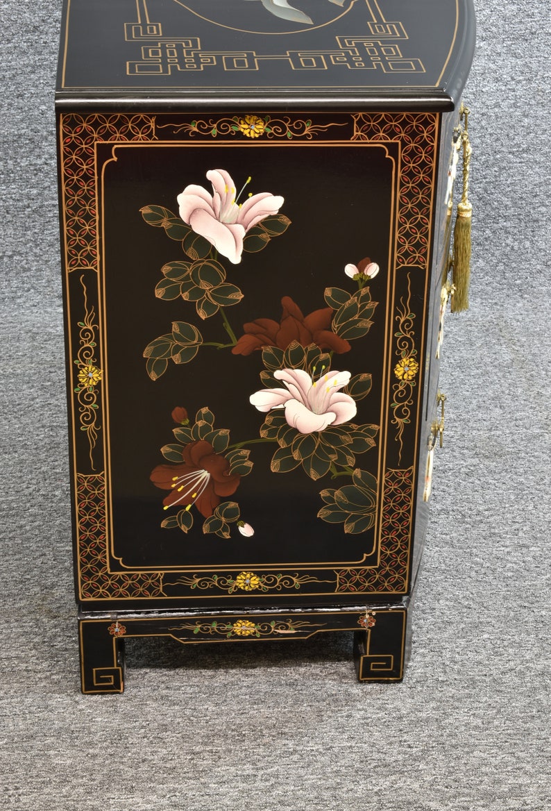 Pode incluir: Arm&aacute;rio lacado de preto com design floral. O arm&aacute;rio tem um motivo floral com flores rosa, brancas e marrons sobre um fundo preto. O arm&aacute;rio tem detalhes dourados e uma borla decorativa.