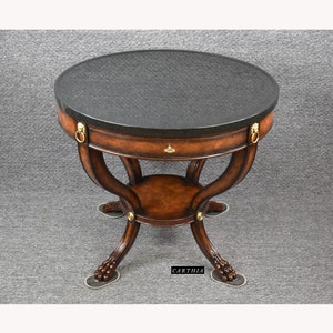 May include: A round, dark wood table with a black granite top. The table has a single drawer with brass lion head pulls and four legs with paw feet. The table is 30 inches in diameter.