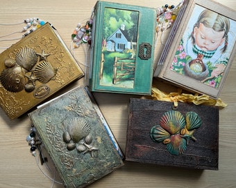 Könnte beinhalten: Fünf dekorative Journale mit verschiedenen Einbänden. Die Einbände zeigen ein Muschel-Design, ein Haus mit einem Zaun, ein Mädchen mit einem Vogel, ein Muschel-Design und ein Muschel-Design.