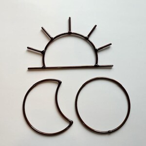 May include: Three dark brown metal celestial shapes: a sun with rays, a crescent moon, and a full moon. The sun is a semicircle with vertical lines extending upwards. The moon shapes are simple, minimalist designs.