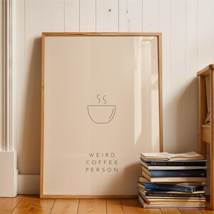 May include: A framed print with a beige background and a black line drawing of a steaming cup of coffee. The text "Weird Coffee Person" is printed below the image.