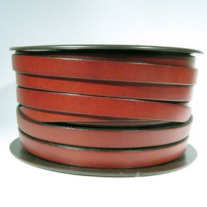 May include: A roll of red leather cord with a black edge. The cord is wound around a brown spool.