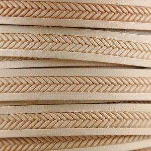 May include: Close-up of beige leather cord with a woven pattern. The cord is stacked in layers, showing the detail of the woven design.