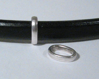 May include: Two silver metal rings, one is a flat ring and the other is a slightly thicker ring with a rounded edge. The rings are on a black leather background.