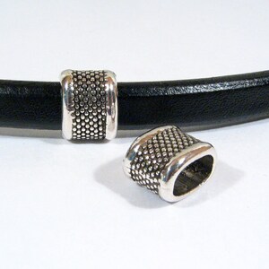 May include: Two silver metal end caps for leather bracelets. The end caps have a textured surface and a rounded shape.