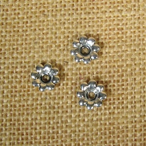 May include: Three silver flower-shaped metal bead caps with a hole in the center.