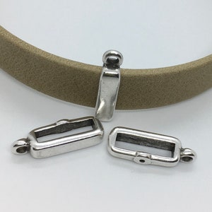 Op de afbeelding: Drie zilverkleurige metalen gespen voor leren banden. Elke gesp heeft een rechthoekige opening en een kleine lus aan één uiteinde.