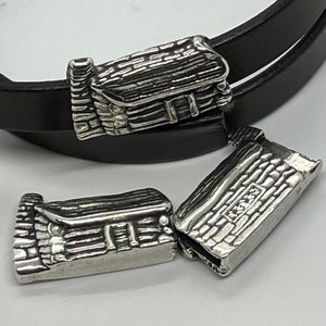 May include: Three silver-toned metal charms shaped like log cabins. The charms have a rustic, textured design and are perfect for adding a touch of charm to a bracelet or necklace.