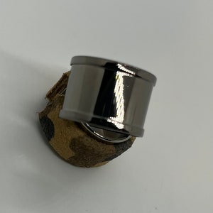 Puede incluir: Un anillo de metal negro con una superficie redonda y lisa. El anillo está sobre una superficie con un patrón marrón y negro.