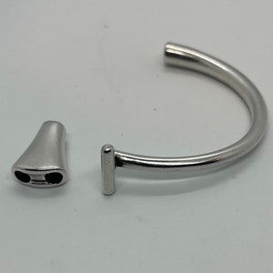 May include: A silver bracelet with a unique clasp design. The clasp is a separate piece that fits into the bracelet.