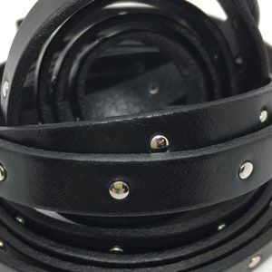 May include: Black leather strap with silver studs. The strap is rolled up and the studs are visible on the edges.