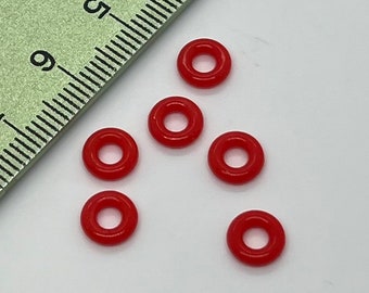 May include: Six red plastic jump rings. The rings are approximately 1.2 cm in diameter.