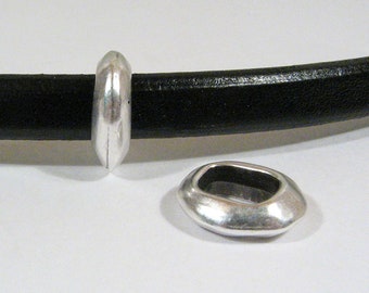 May include: Two silver-colored oval-shaped jewelry findings. One is attached to a black leather band, and the other is separate. The findings have a smooth, polished finish and a hollow interior. The band is approximately 0.5 inches in diameter.