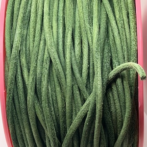 May include: A spool of olive green round leather cord wrapped tightly around a bright pink plastic core. The cord features a matte, textured surface and a consistent cylindrical shape, showing multiple parallel strands wound together in a dense coil.