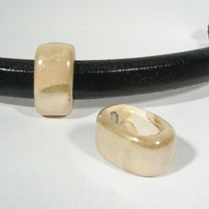 May include: Two off-white ceramic beads with a glossy finish. The beads are round and have a hole in the center. The beads are on a white surface.