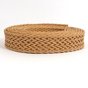 May include: A close-up of a brown braided cord, coiled into a circle. The cord is made of a woven material, creating a textured and intricate pattern.