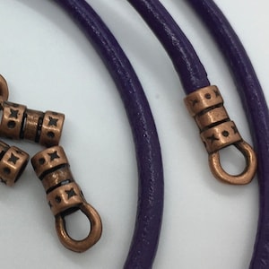 May include: Purple leather cord with copper end caps. The end caps have a decorative design.
