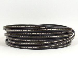 May include: Black leather cord with white stitching. The cord is rolled up and is approximately 1.2 cm wide.