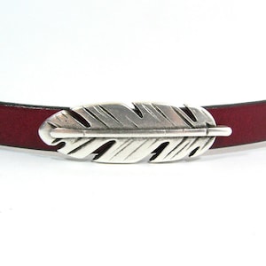 May include: A burgundy leather belt with a silver feather buckle.
