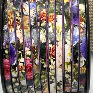Può includere: Un rotolo di nastro viola e nero con una stampa floreale che presenta una varietà di fiori in tonalità di rosa, bianco e blu.