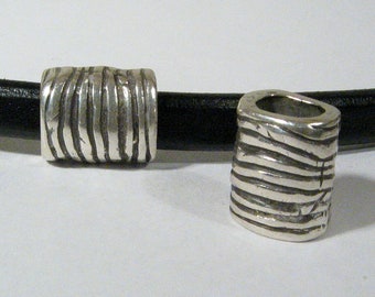 May include: Two silver metal beads with a textured, wavy design. The beads are on a black leather cord.
