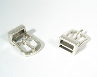 May include: Two silver metal belt buckles. One buckle is closed and the other is open.