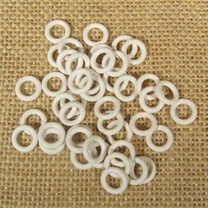 May include: A pile of white plastic jump rings, also known as split rings, on a burlap background. These rings are used for connecting jewelry components.