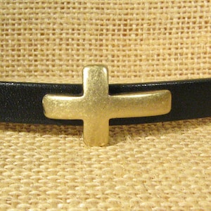 Peut inclure: Un bracelet en cuir noir avec un charme en forme de croix dorée.