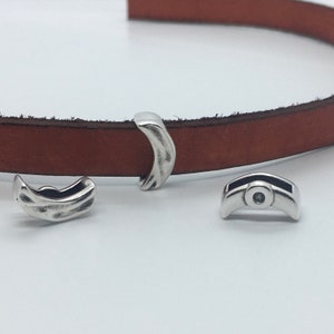 May include: Three silver metal clasps for leather straps. The clasps are in the shape of a crescent moon. One clasp has a small round hole in the center.