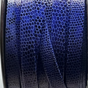 以下が含まれることがあります： 爬虫類のような質感の青い革紐の巻き取り機のクローズアップ。紐は濃い青色で、濃い影がグラデーション効果を生み出しています。質感はヘビやトカゲの鱗に似ています。