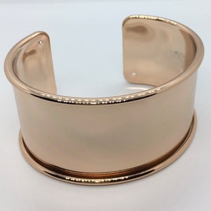 Peut inclure: Un bracelet large en or rose avec une finition lisse et polie. Le bracelet a une forme légèrement incurvée et un design simple et moderne.