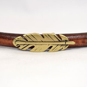 May include: A brown leather bracelet with a gold-toned feather charm.