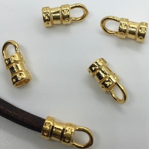 May include: Five gold-toned metal cord end caps with a decorative design. Each end cap has a small loop at the top.