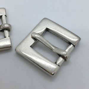 May include: Silver metal buckle with a square shape and a smooth finish.