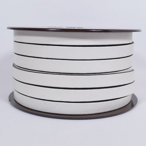 May include: A roll of white and black striped ribbon. The ribbon is wound around a brown spool.