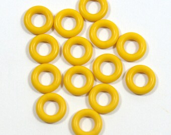 May include: A group of 15 yellow rubber rings, arranged in a loose pile on a white surface.