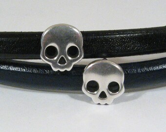 May include: Two silver skull charms on a black leather bracelet.