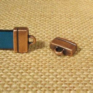May include: Two copper-colored metal clasps for leather straps. The clasps have a rectangular shape with a small loop on one end.