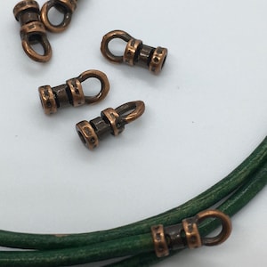 May include: Five antique copper-toned metal cord end caps with a loop on one end. The cord end caps are shown on a green leather cord.